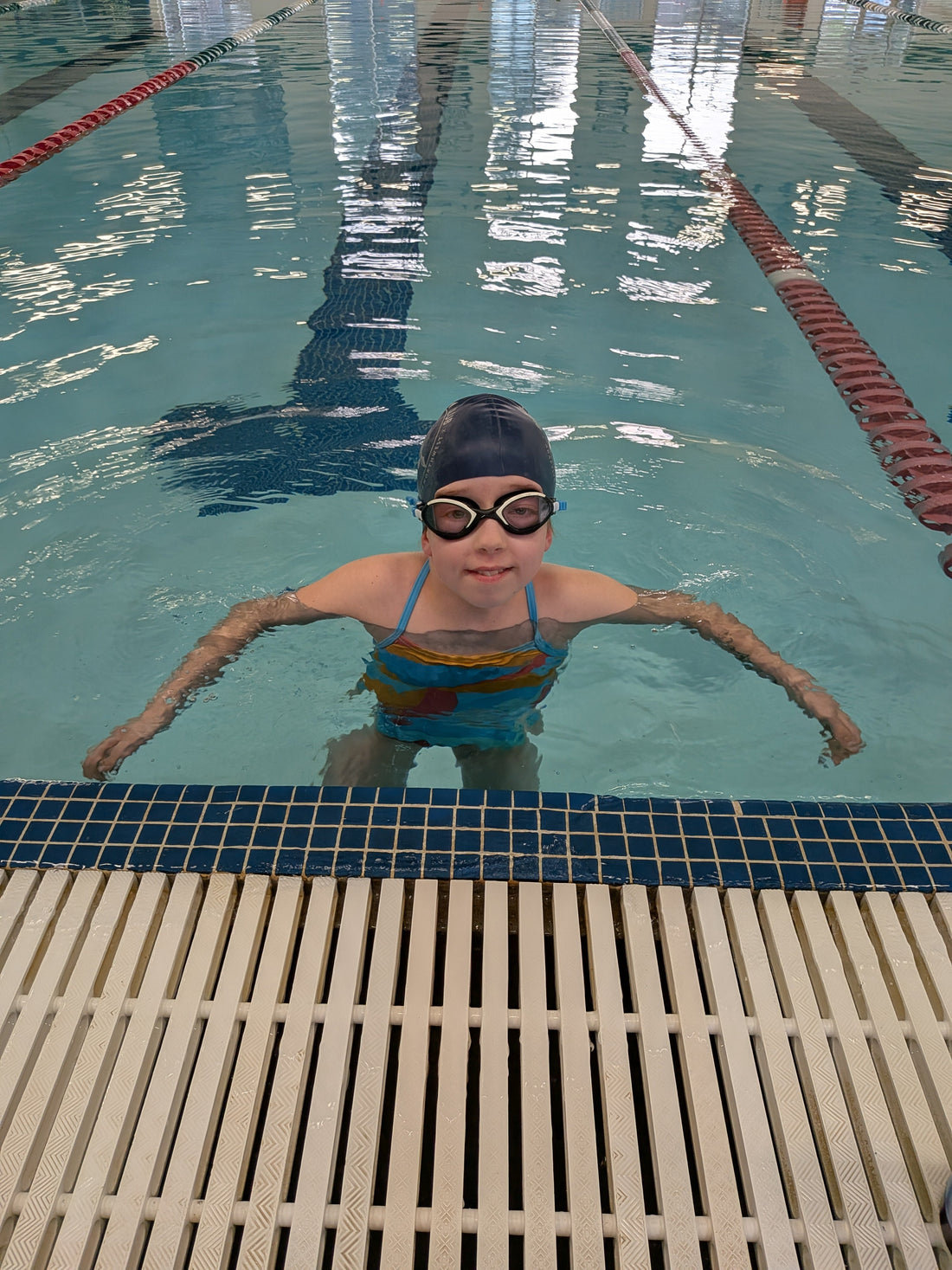 Child in a swimming pool wearing goggles and a swim cap.